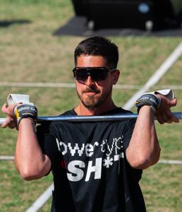 Athlete lifting weights outdoors, wearing sunglasses and sporting a motivational shirt.