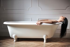 Woman with long hair relaxing in a vintage white bathtub in a minimalist bathroom.